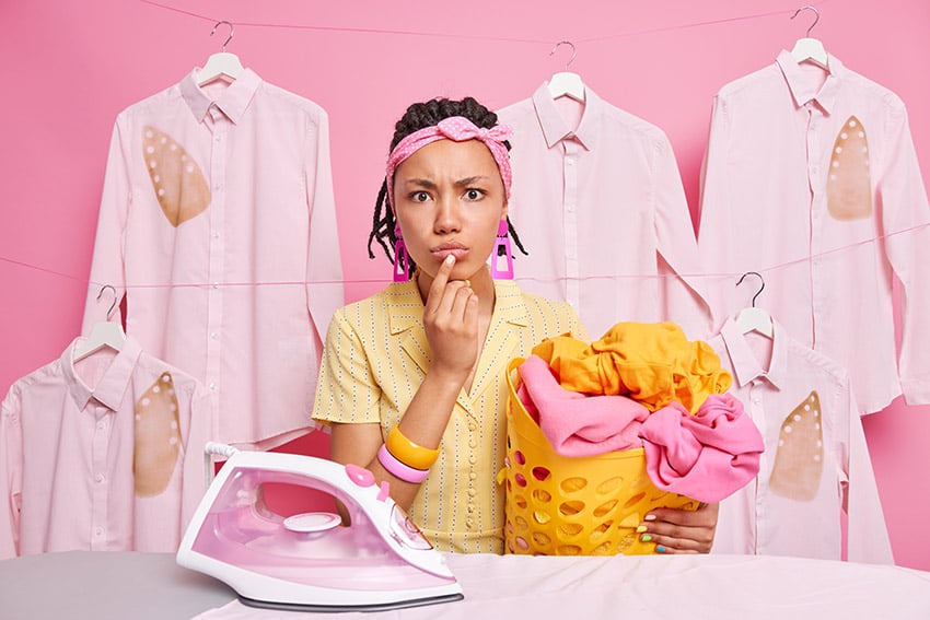 Người phụ nữ trẻ da đen chăm chú nghiêm túc cầm giỏ đầy quần áo đã giặt là bàn là vải lanh nhìn về phía dir